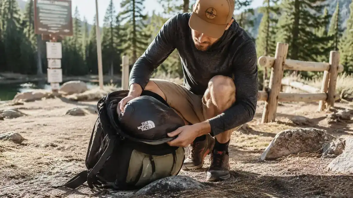 Hiker stuffing a compressed sleeping bag into a backpack at a trailhead