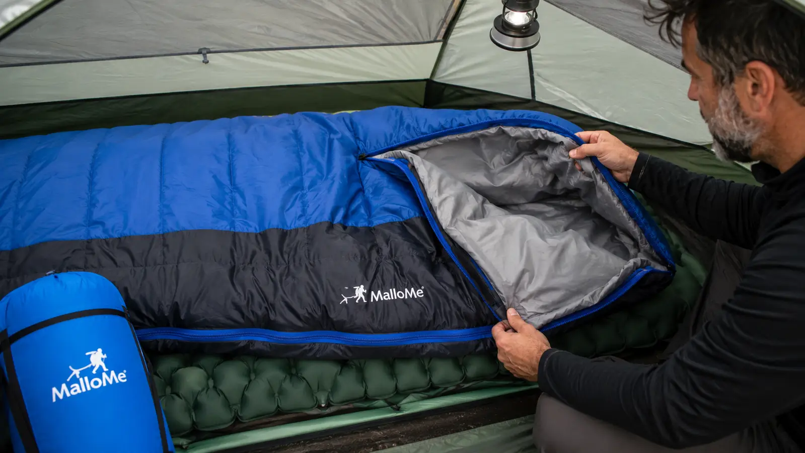 MalloMe mummy sleeping bag unrolled and laid out on a sleeping pad inside a tent, zipper pulled halfway